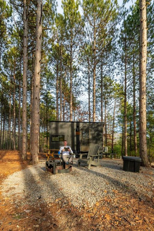 a man sitting in front of a tiny house in the woods at Postcard Cabins Wild Rose, Outdoor Collection by Marriott Bonvoy in Wild Rose