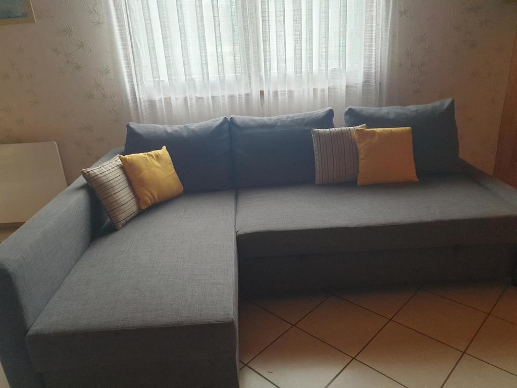 a couch with pillows on it in front of a window at Logement du Bois de Chaubon in Fillinges