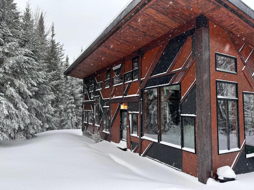 ein schneebedecktes Gebäude mit Bäumen im Hintergrund in der Unterkunft The Sculptural Nature Escape, hot tub, Billiards in Val-David