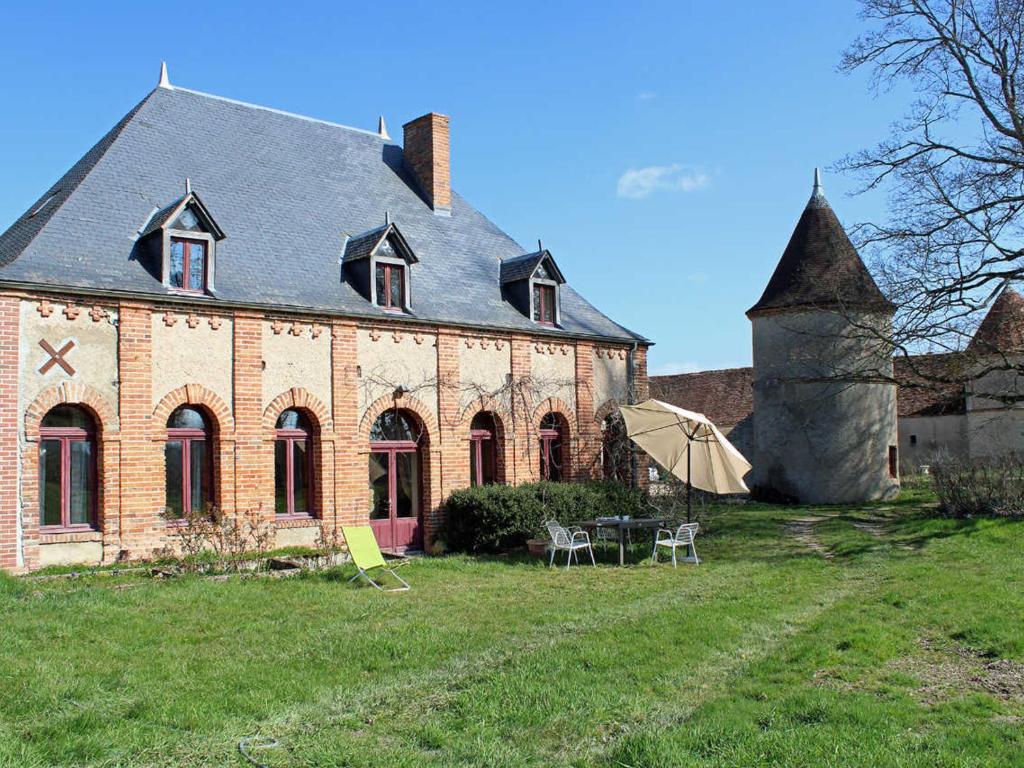 een oud bakstenen gebouw met een tafel en een paraplu bij Gîte lumineux dans ancienne orangerie avec jardin et barbecue - FR-1-489-281 in Trézelles