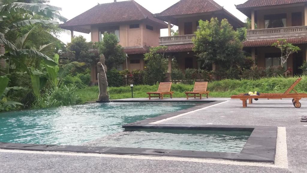 a pool in front of a building with two benches at Arjana Bungalows Rice Field in Ubud