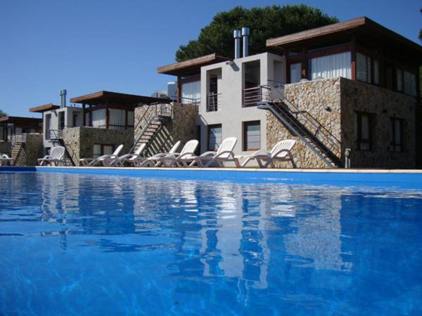 a swimming pool with chairs and a house in the background at Cabañas Arenas Blandas in Villa Gesell