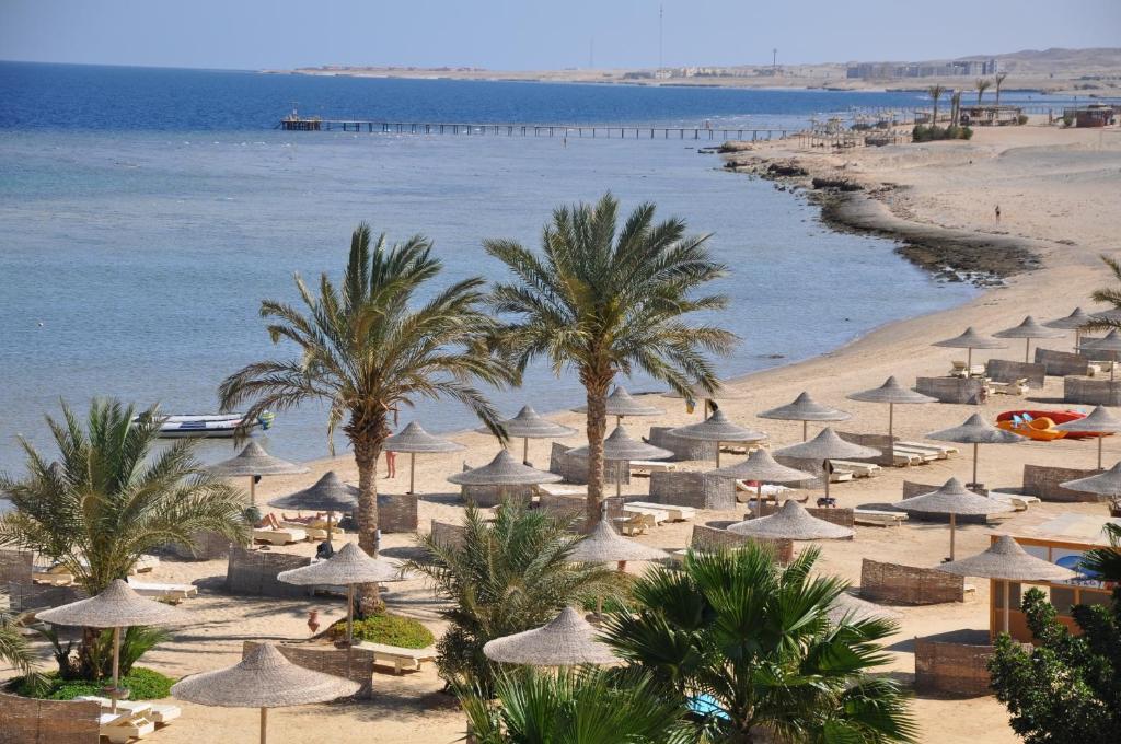 a beach with umbrellas and palm trees and the ocean at Shoni Bay Resort in Marsa Alam City
