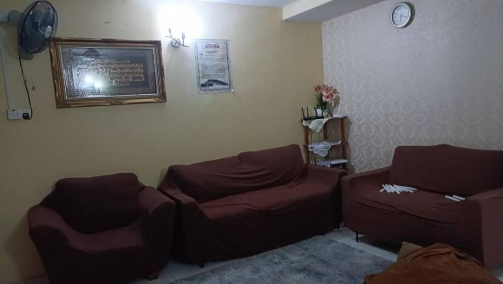 a living room with two brown couches and a clock at el-yusra homestay in Bayan Lepas