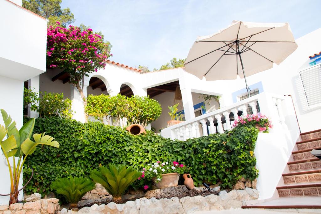 een wit huis met bloemen en een paraplu bij Villa Cala Xuclar in Portinatx