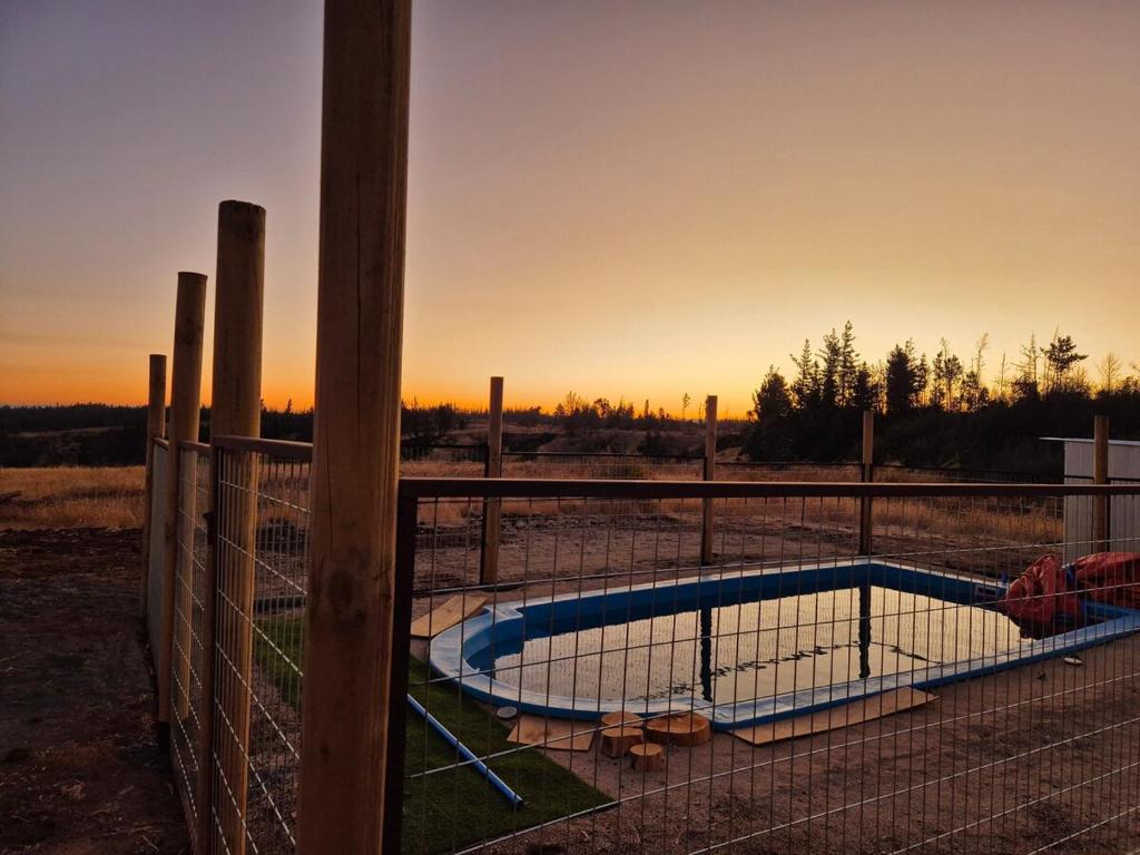 a fence with a swimming pool in a field at Hermosa Cabaña en medio de la naturaleza in Los Angeles