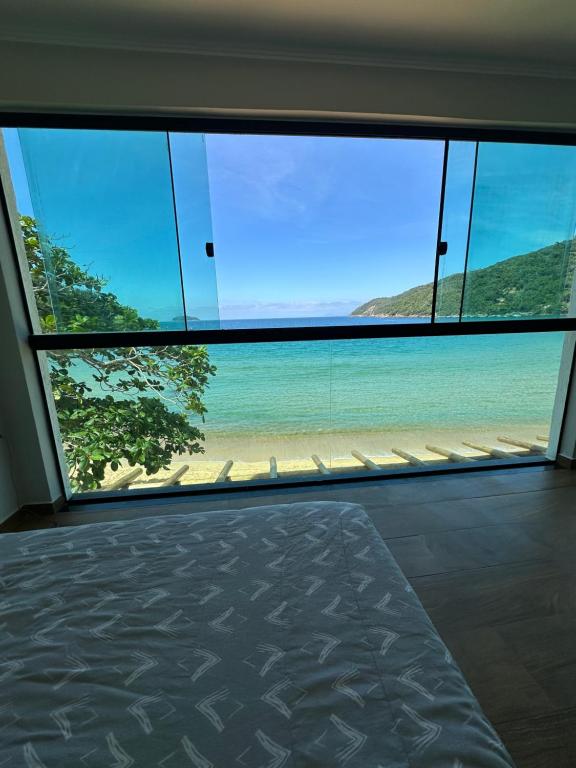 a bedroom with a view of the beach from a large window at Duplex beira mar ilha grande proveta in Angra dos Reis
