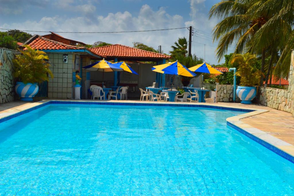 a swimming pool with chairs and tables and umbrellas at Chalés Pontal da Ilha in Itamaracá
