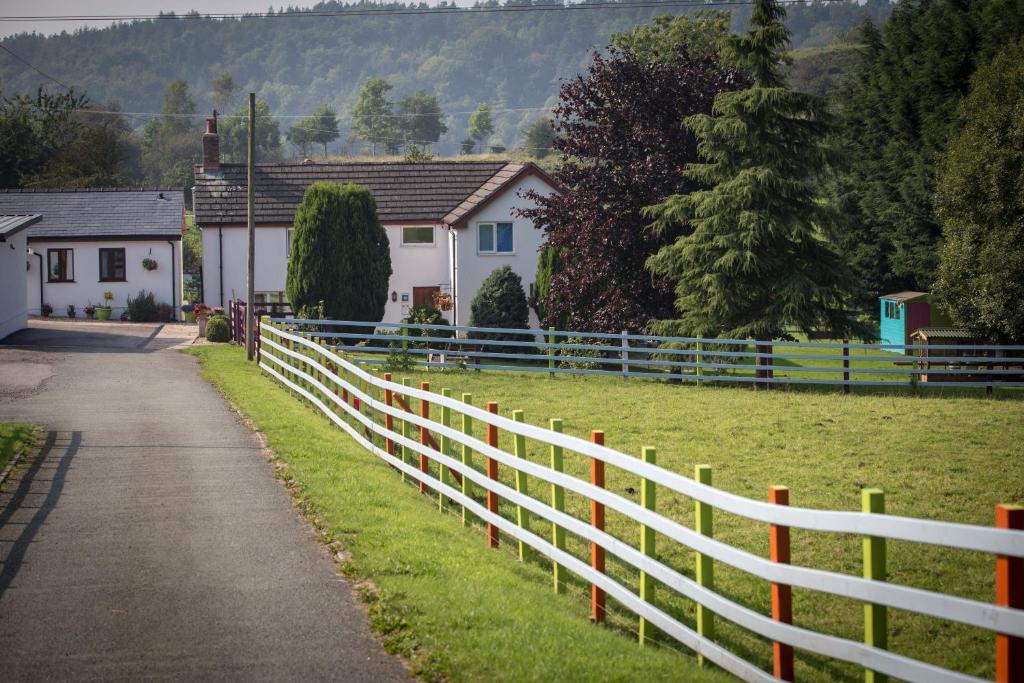 a white fence next to a field with houses at Glan Llyn Farm House in Mold