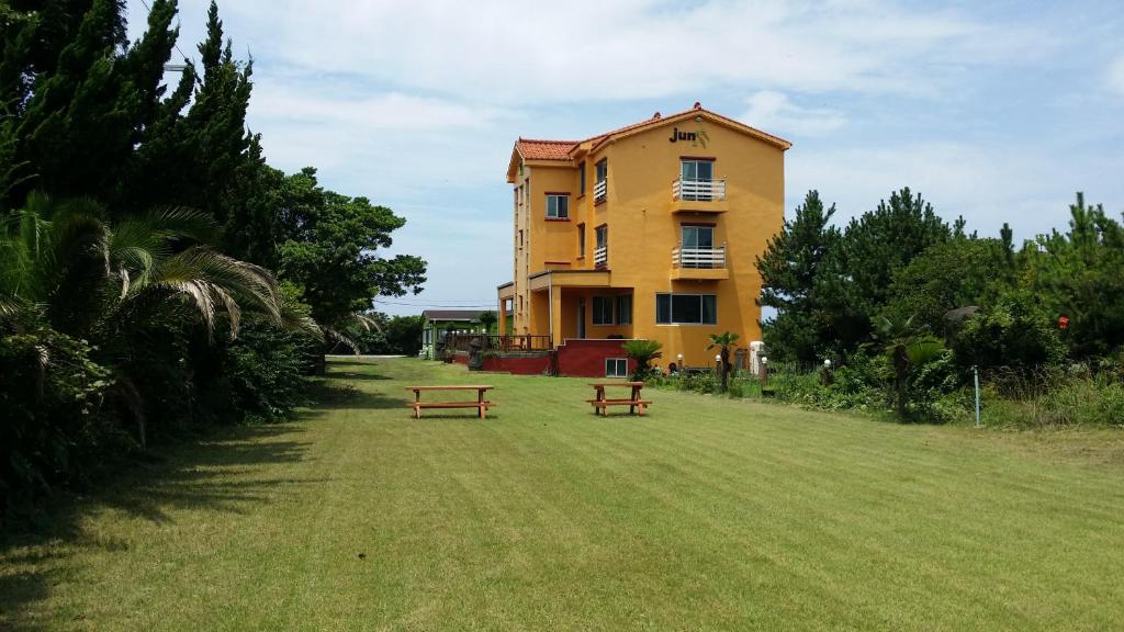 un edificio amarillo con dos bancos delante en Jun House en Jeju