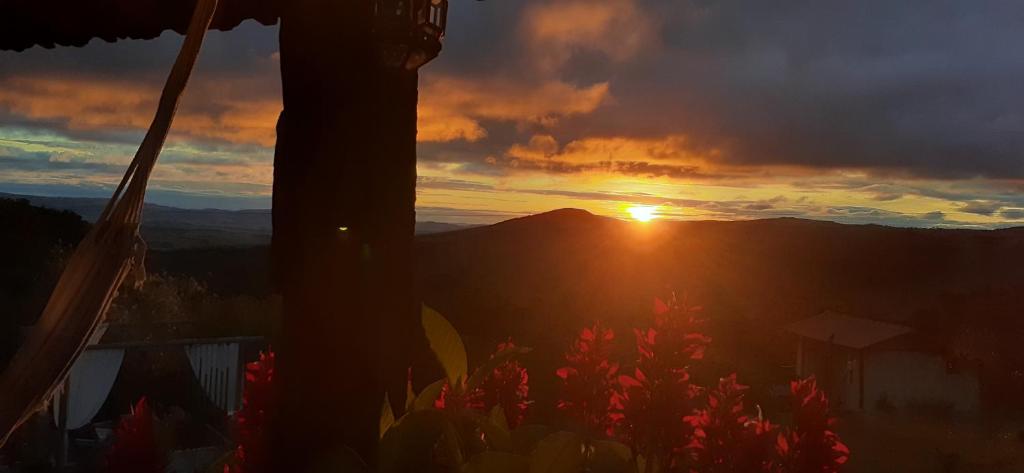 einen Sonnenuntergang in den Bergen mit Blumen im Vordergrund in der Unterkunft Pousada Canto da Lua - Charme, exclusividade e linda vista! in Carrancas