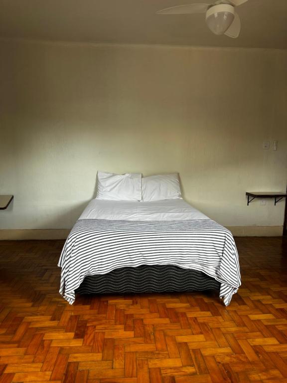 a bed with white sheets and pillows on a wooden floor at Oxx Quarto Terra in Congonhas