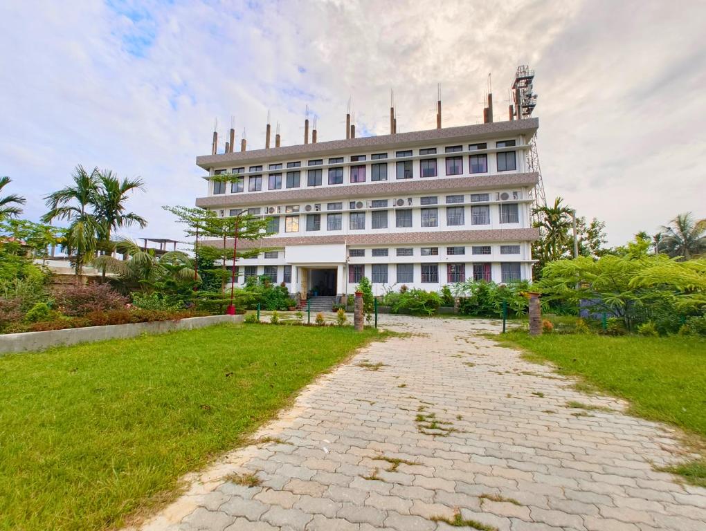 a large white building with a grass field in front of it at Taj Heritage Hotel and Restaurant - Premium & Budget Rooms in Jorhāt