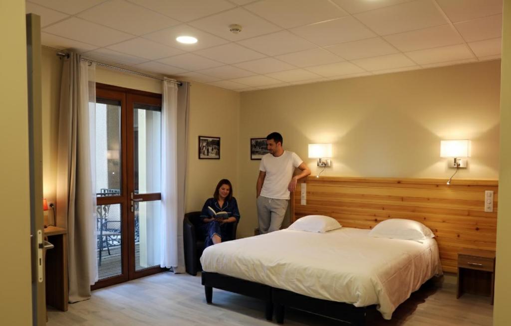 Ein Mann und eine Frau in einem Schlafzimmer mit einem Bett in der Unterkunft Hôtel Belleville in Lamalou-les-Bains