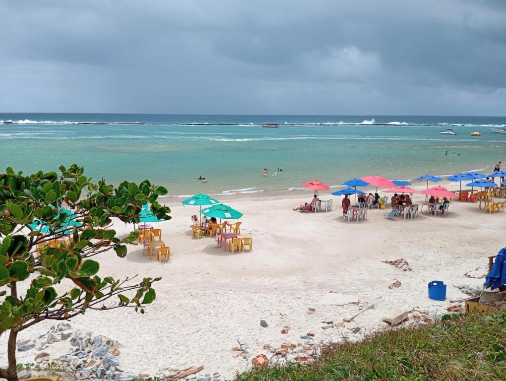 a beach with tables and umbrellas and people in the water at Pousada da Sol na Praia do Frances in Praia do Frances