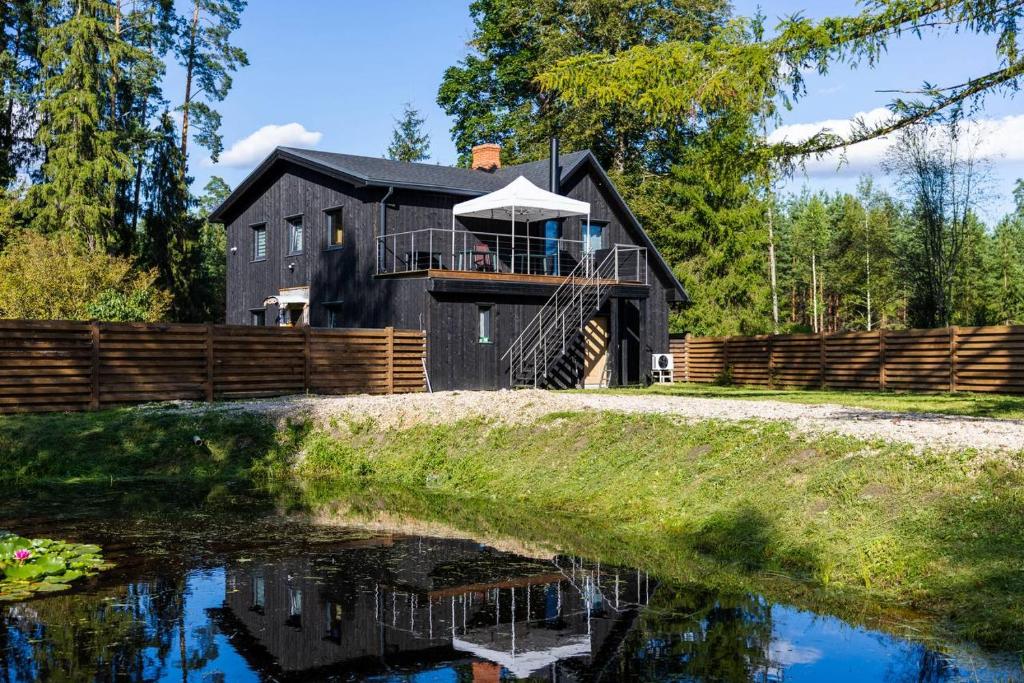 een zwart huis met een balkon en een vijver bij Dailes in Dzelmes