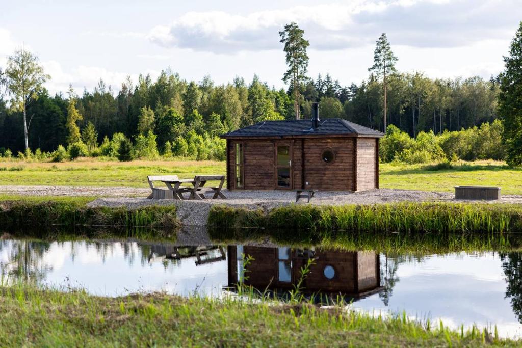 ein kleines Gebäude neben einem Teich mit einem Picknicktisch in der Unterkunft Cope un Pirts in Yumprava