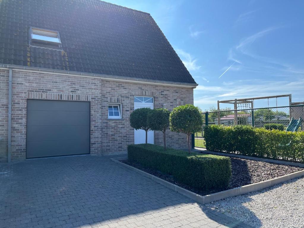 a brick house with a garage and some bushes at Huis Marlin in De Haan