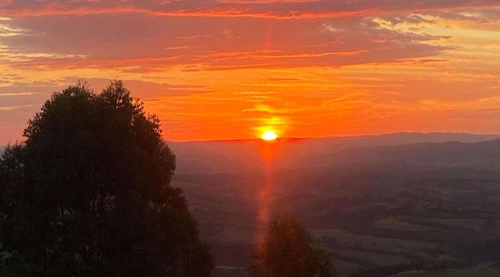 een zonsondergang in de bergen met een boom op de voorgrond bij Suíte 3 Centro São Thomé das Letras in São Thomé das Letras