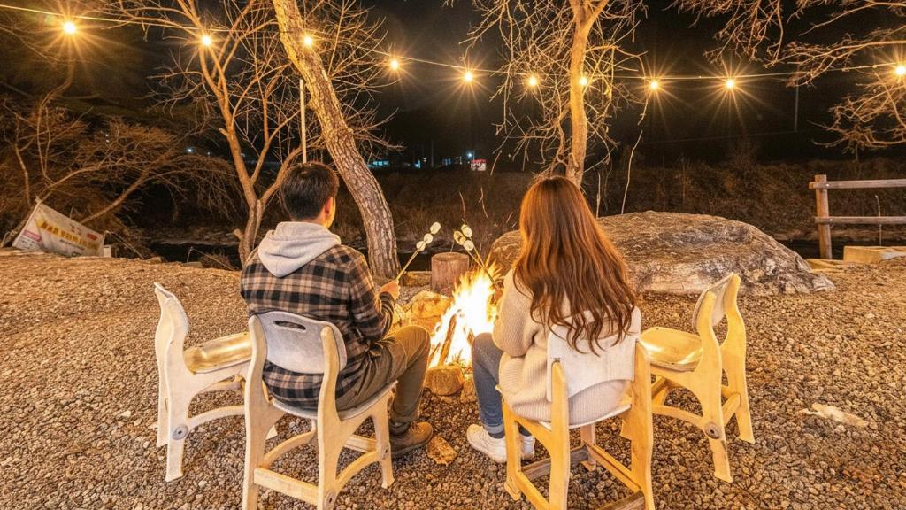Zwei Leute sitzen nachts um ein Feuer herum in der Unterkunft Yangpyeong Smile Caravan Pension in Yangpyeong
