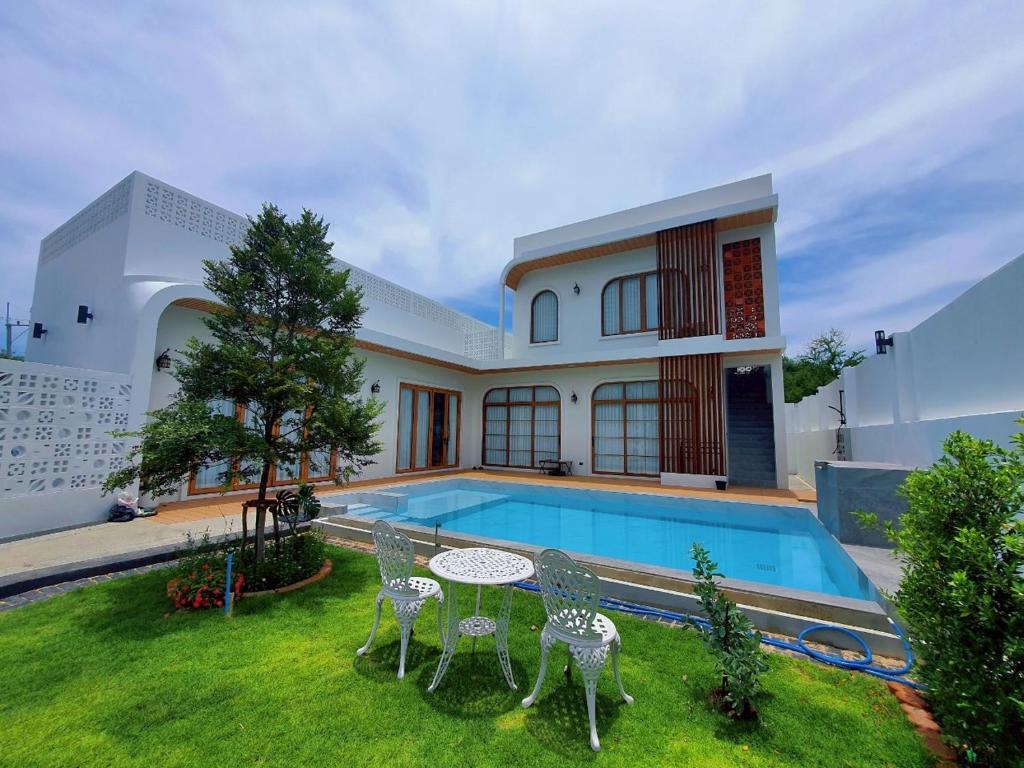 een huis met een zwembad en een tafel en stoelen bij Villanarachaam in Cha Am