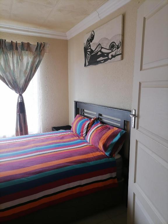 a bedroom with a bed with colorful pillows and a window at Imvumbu Guest House in Nelspruit