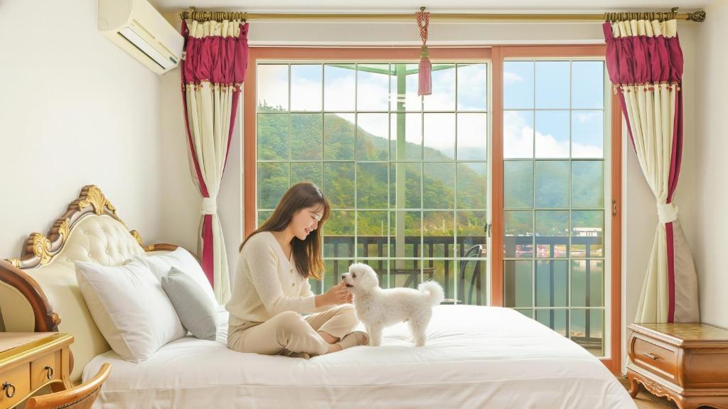 een vrouw zit op een bed met een klein wit hondje bij Gapyeong Elin Pension in Gapyeong