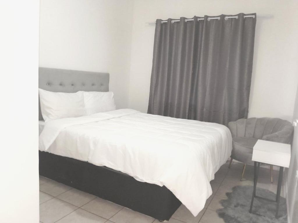 een slaapkamer met een wit bed en een stoel bij The Nexus Suites in Gaborone
