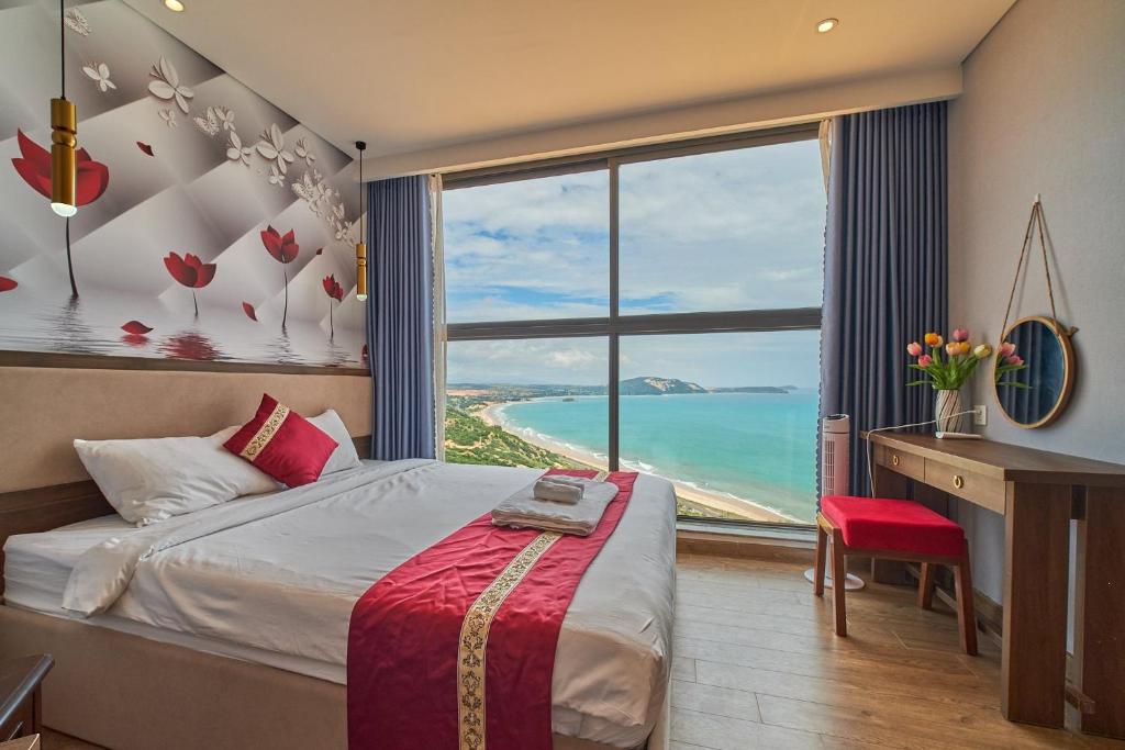 a bedroom with a bed and a desk and a large window at APEC Mandala Mũi Né VIP in Mui Ne