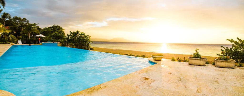 una piscina accanto a una spiaggia con il tramonto di Hispaniola Luxury Ocean Front Condo a Sosúa