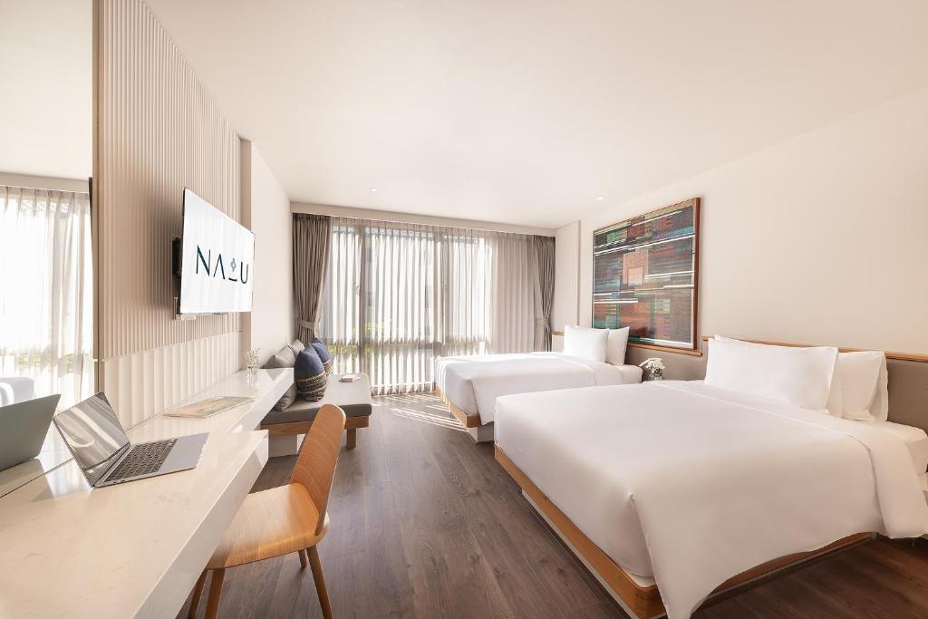 a hotel room with two beds and a desk with a laptop at Na U Hotel in Chiang Mai
