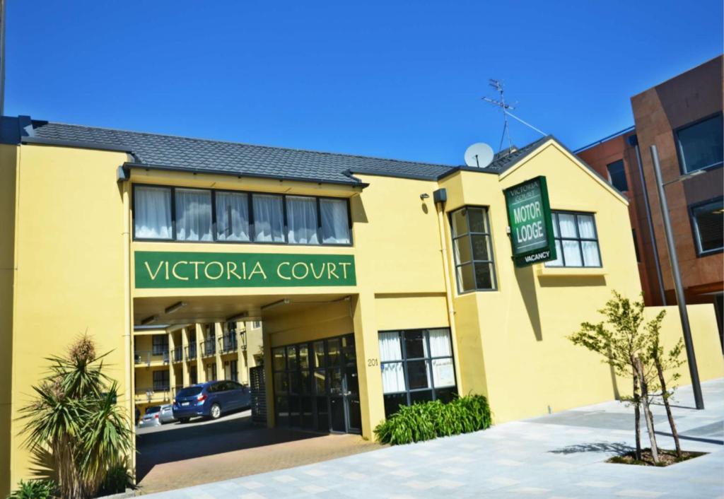 Victoria Court Motor Lodge في ويلينغتون: مبنى أصفر مع علامة لملعب vctoria