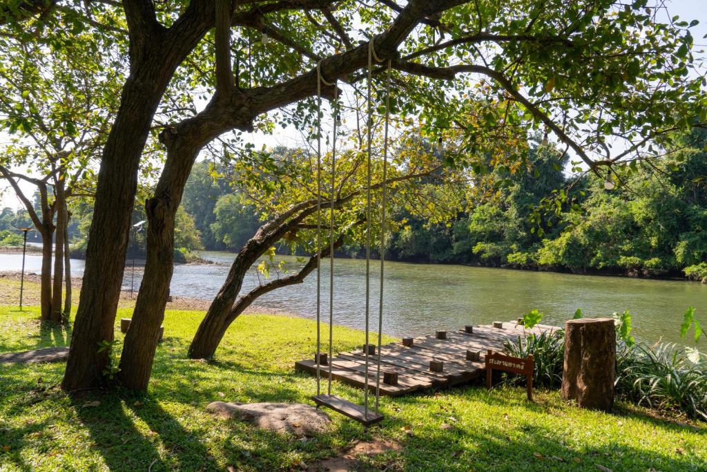 een schommel hangend aan een boom naast een rivier bij Comsaed River Kwai Resort in Kanchanaburi