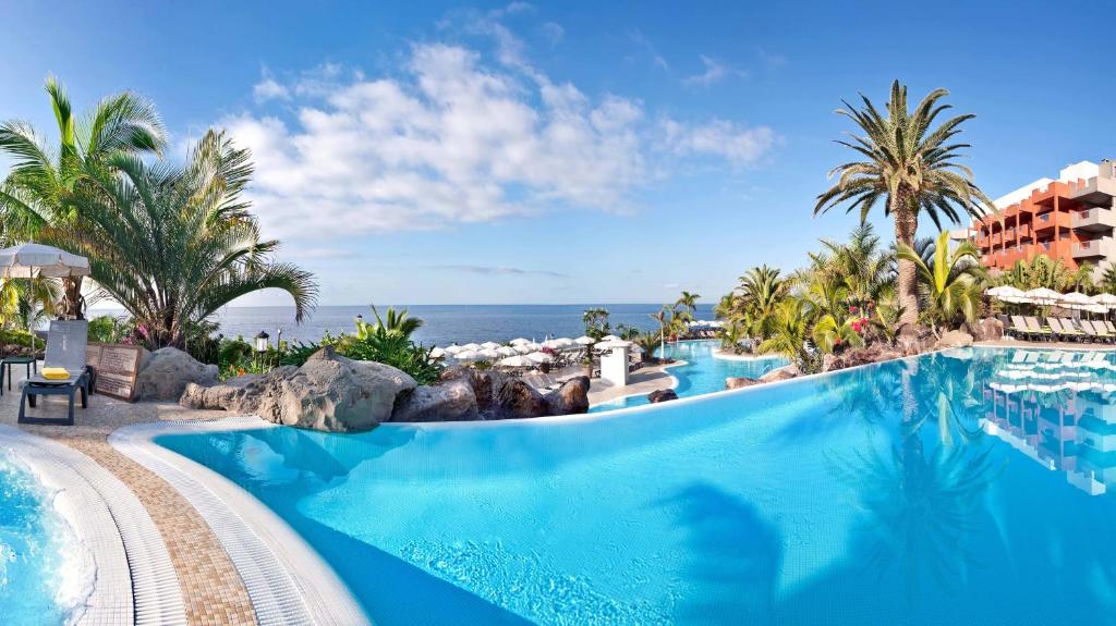 une piscine dans un complexe avec l'océan en arrière-plan dans l'établissement Adrián Hoteles Roca Nivaria, à Adeje
