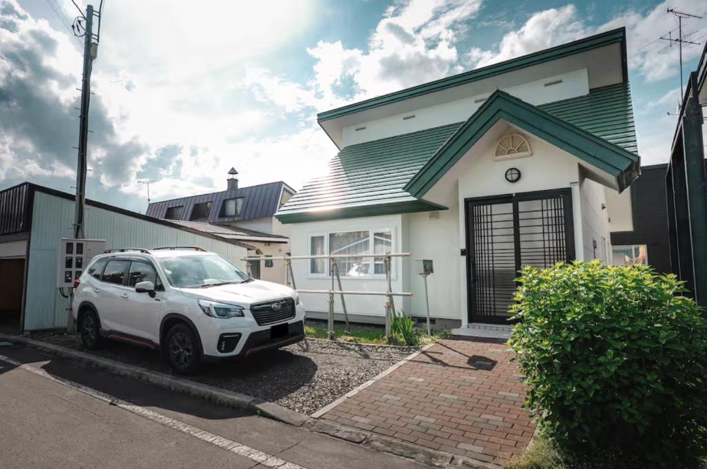 une voiture blanche garée devant une maison blanche dans l'établissement 南町ハウス, à Biei