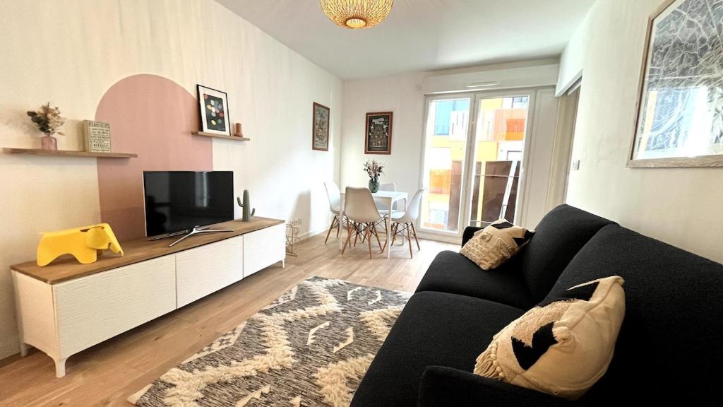 een woonkamer met een zwarte bank en een flatscreen-tv bij Le Cours des Arts in Nantes