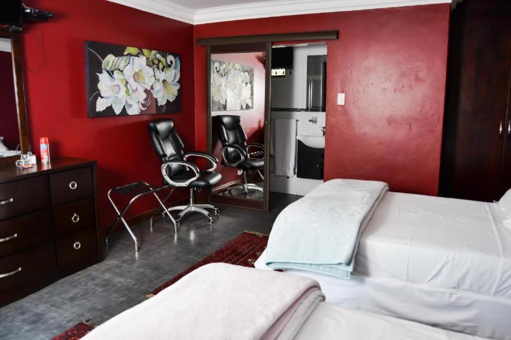 a bedroom with red walls and two beds and chairs at Casadeross Guest House in Pretoria