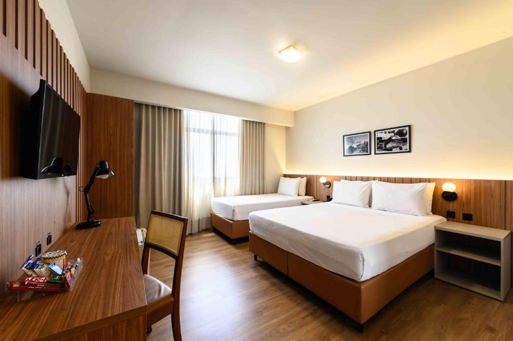 a hotel room with two beds and a desk at Vitoria Praia Hotel in Vitória