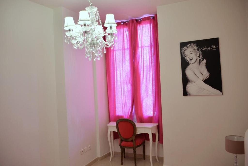 ニースにあるApartment on Rue De France 4のピンクのカーテン、テーブル、シャンデリアが備わるダイニングルーム