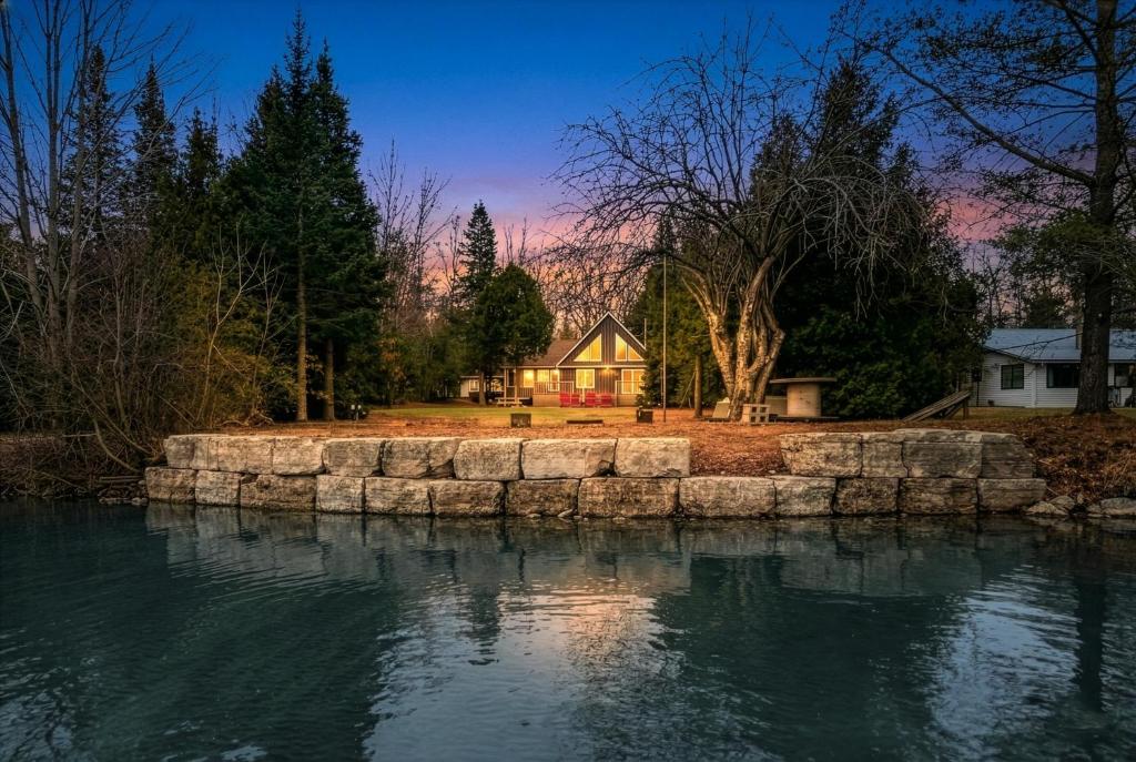 a house with a stone wall next to a body of water at Lakeview Loft A-Frame Escape Tobermory With AC in Tobermory