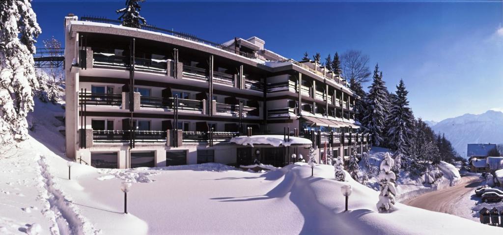 un grand bâtiment dans la neige avec des arbres enneigés dans l'établissement Hôtel de la Forêt, à Crans-Montana