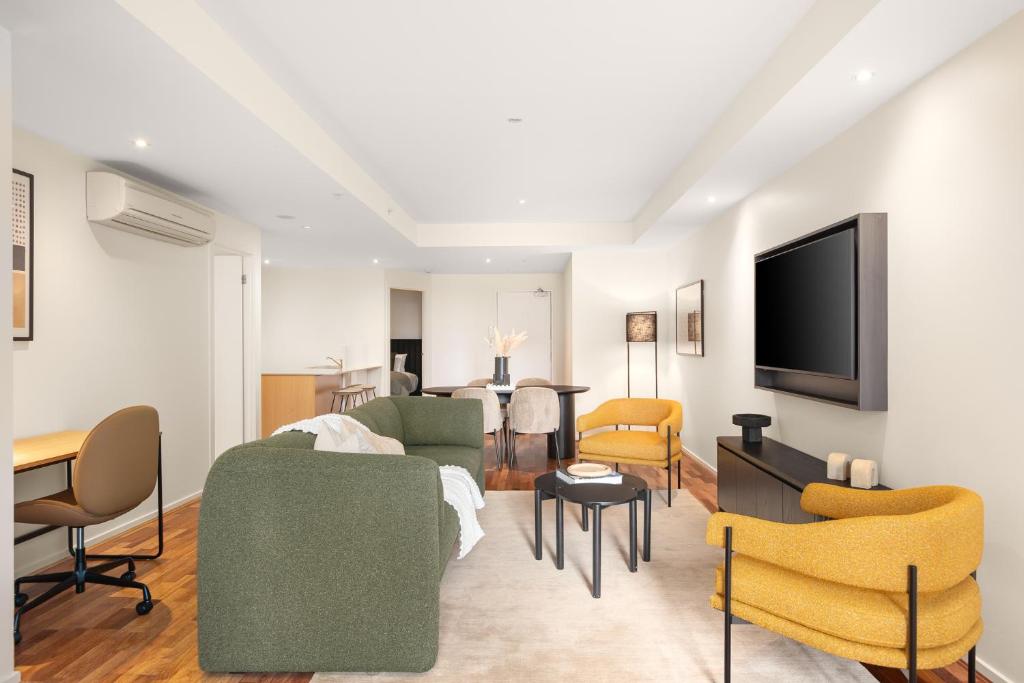 a living room with a couch and chairs and a tv at Nolo Apartments Lonsdale St in Melbourne