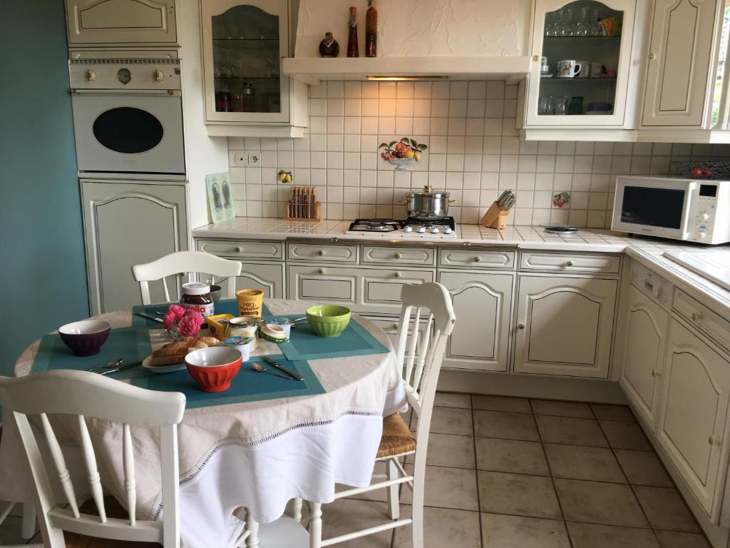 una cocina con mesa y sillas y una cocina con armarios blancos. en La Maison D'Eliane en Aire-sur-la-Lys