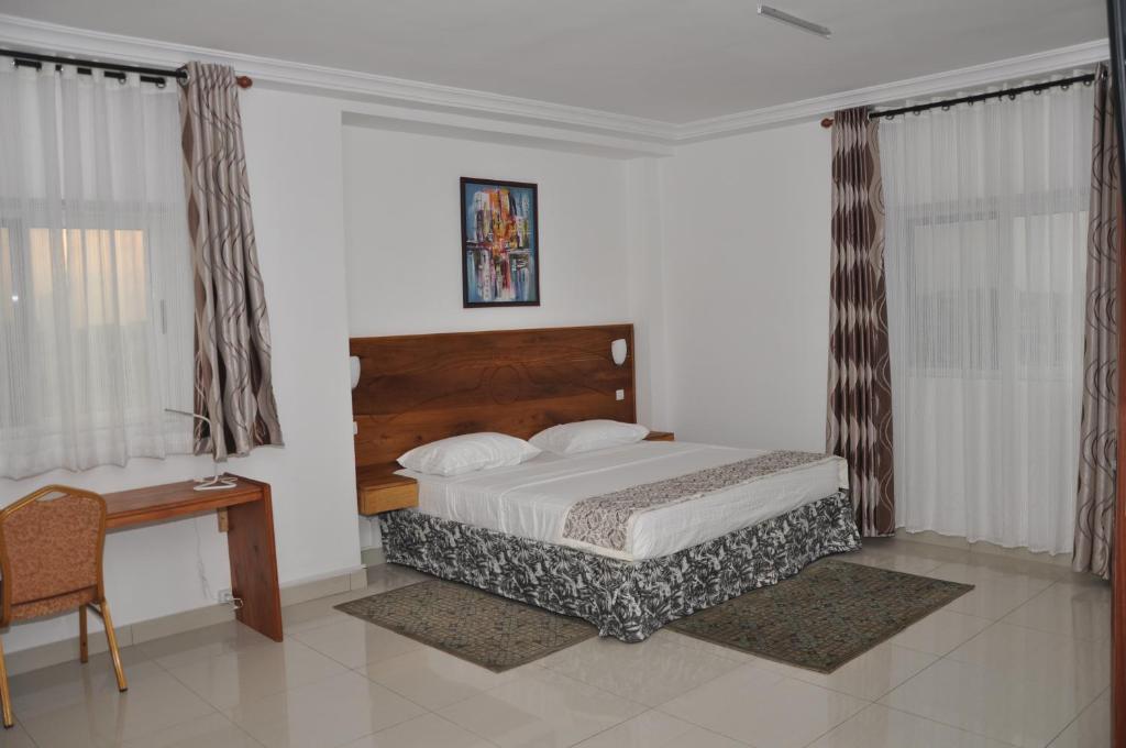 a bedroom with a bed and a desk and curtains at Rosalie's Suites in Lomé