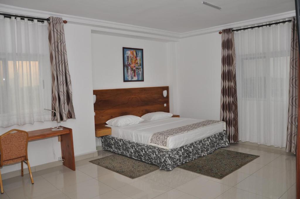 1 dormitorio con cama, escritorio y cortinas en Rosalie's Suites, en Lomé