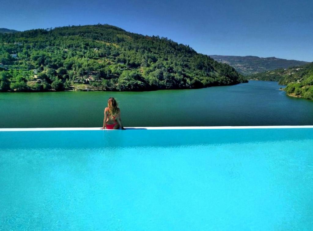 Una donna seduta sul bordo di un grande corpo d'acqua di Douro Royal Valley Hotel & Spa a Ribadouro