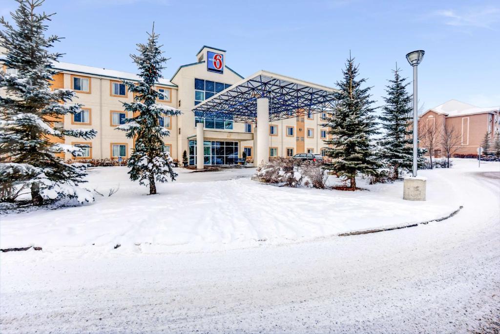 un gran edificio en la nieve con árboles delante en Motel 6-Red Deer, AB, en Red Deer
