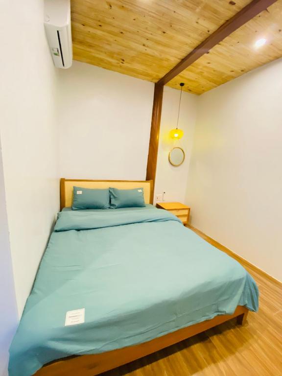 a bedroom with a bed with blue sheets and wooden ceilings at Nhà Dâu Homestay in Muong Cha