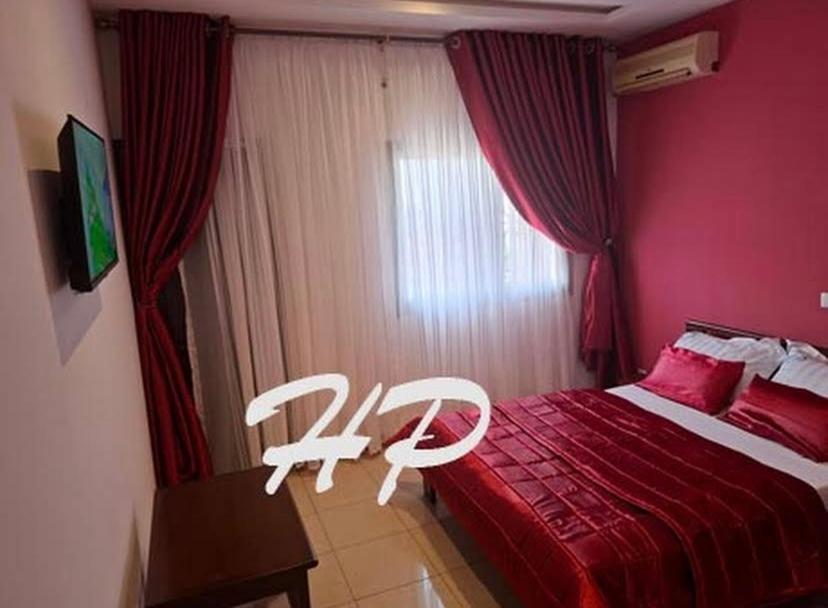 Un dormitorio con una cama roja y una silla blanca. en Hôtel Les Pyramides, en Yaoundé