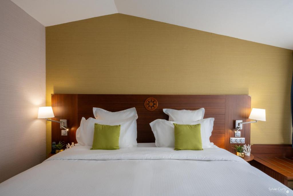 een slaapkamer met een groot wit bed met groene kussens bij Hôtel Le Yachtman, The Originals Collection in La Rochelle